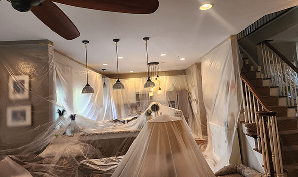 Living room and kitchen area covered in plastic sheets, indicating preparation for painting or renovation work.