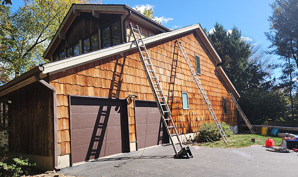 Two ladders leaning against a wooden shingle garage with two brown doors on a sunny day.