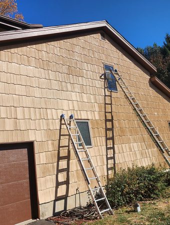 A man is using a ladder to work on the exterior of a house.