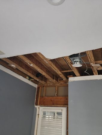 A room with a partially repaired ceiling, showing tools and materials used for the repair process.