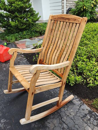 A rocking chair placed on a driveway surrounded by a grassy yard.
