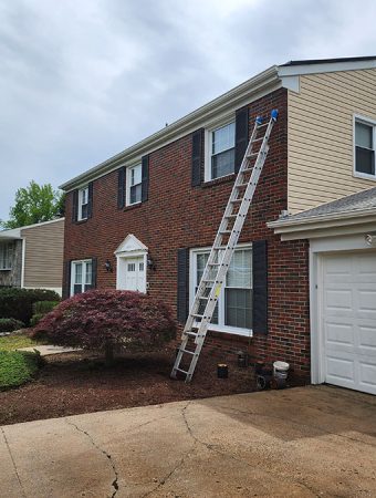 A house featuring a ladder on the roof and a garage door, set against a clear blue sky.